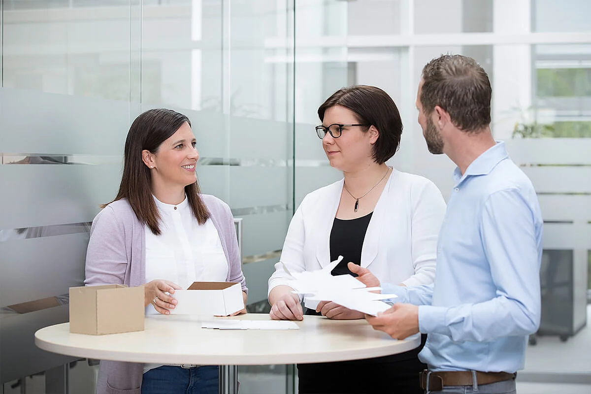 Three colleagues discussing around a table with an open carton in a modern office – SOMIC consulting session